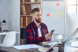 bearded guy using smartphone frony pc his workplace