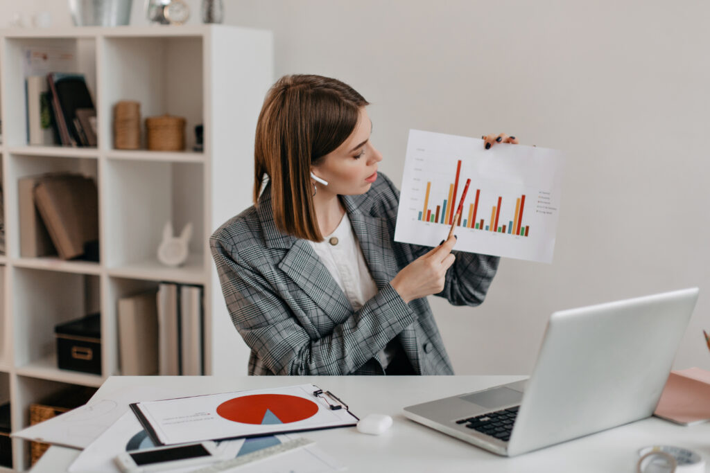 business lady is holding chart her hands telling clients about it through video communication while sitting bright workplace