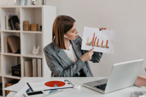 business lady is holding chart her hands telling clients about it through video communication while sitting bright workplace