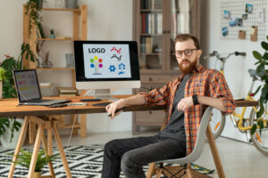 portrait serious handsome bearded brand designer sitting desk with desktop computer laptop home office